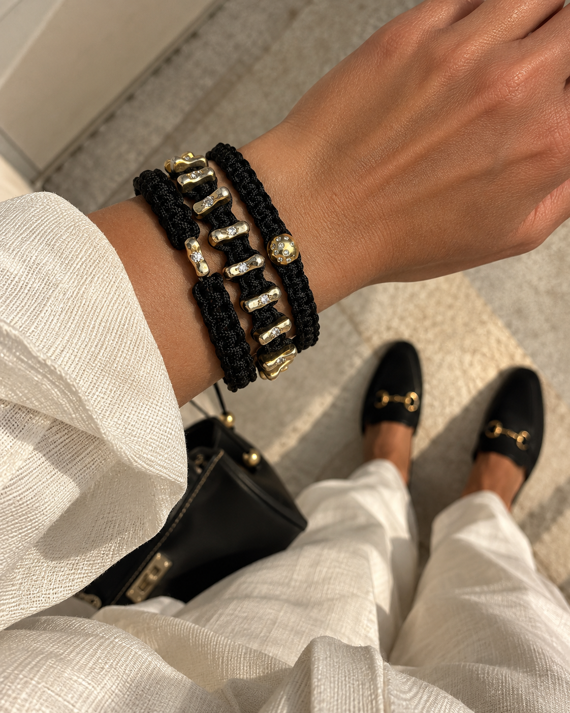 Three AURIAN bracelets stacked on the wrist in black cord and gold