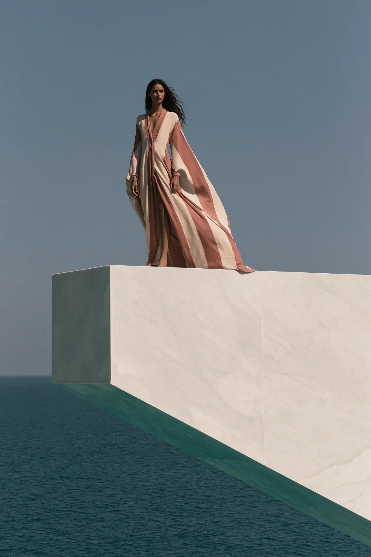 Woman in a striped dress on a white plinth above the sea